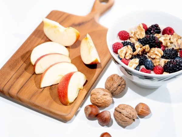 A vibrant breakfast bowl with mixed berries, walnuts, and apple slices on a rustic board.