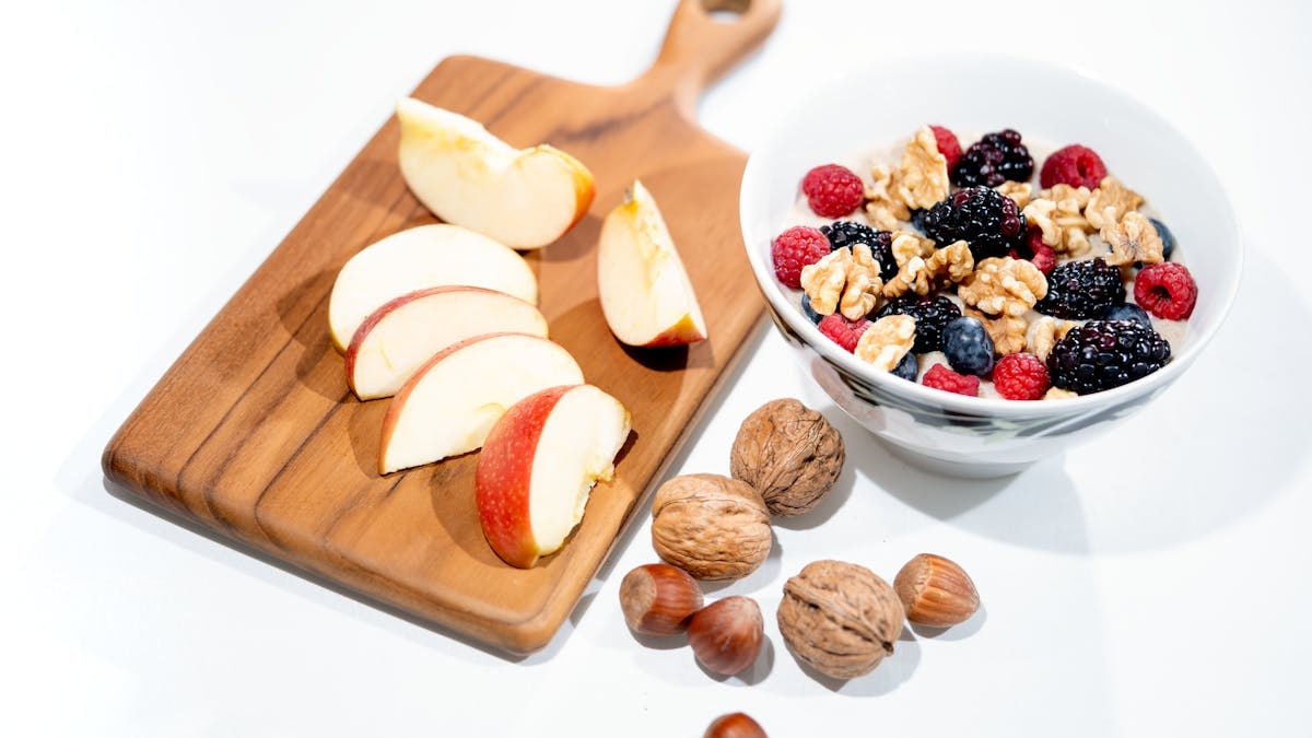 A vibrant breakfast bowl with mixed berries, walnuts, and apple slices on a rustic board.